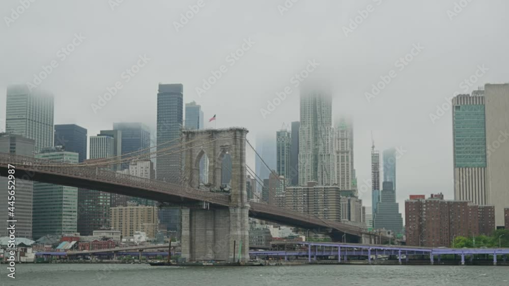 A view of the Brooklyn Bridge and lower Manhattan skyline as seen from the East River on a foggy day.  	