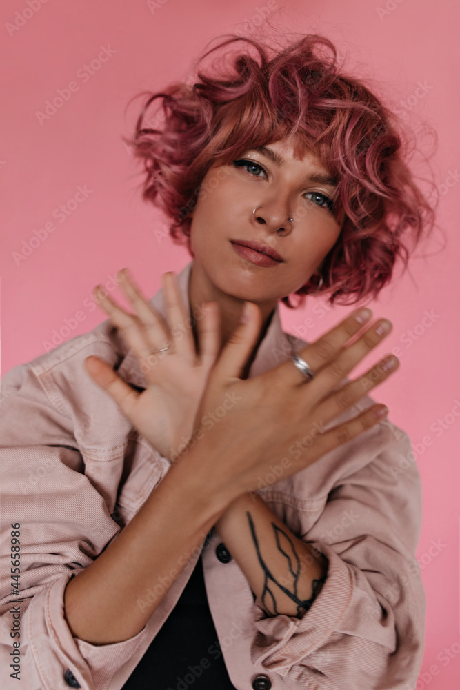 Charming young woman in denim pink jacket moves hands on isolated. Pretty curly girl in black tee poses and looks into camera on pink background. Charming young woman in denim pink jacket moves hands on isolated. Pretty curly girl in black tee poses and looks into camera on pink background.