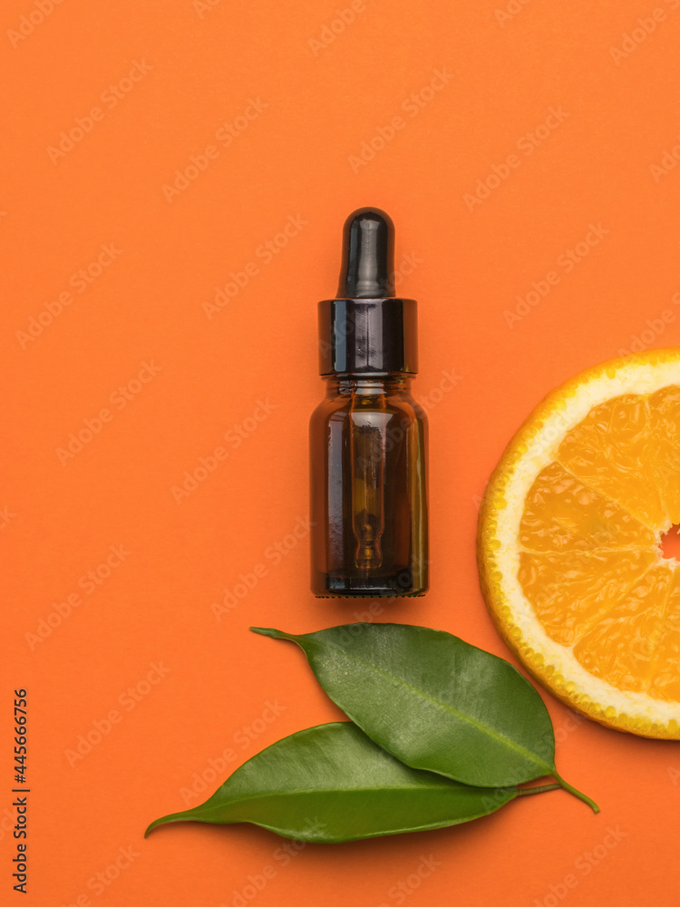 A bottle with an eyedropper, a piece of orange and leaves on an orange background.