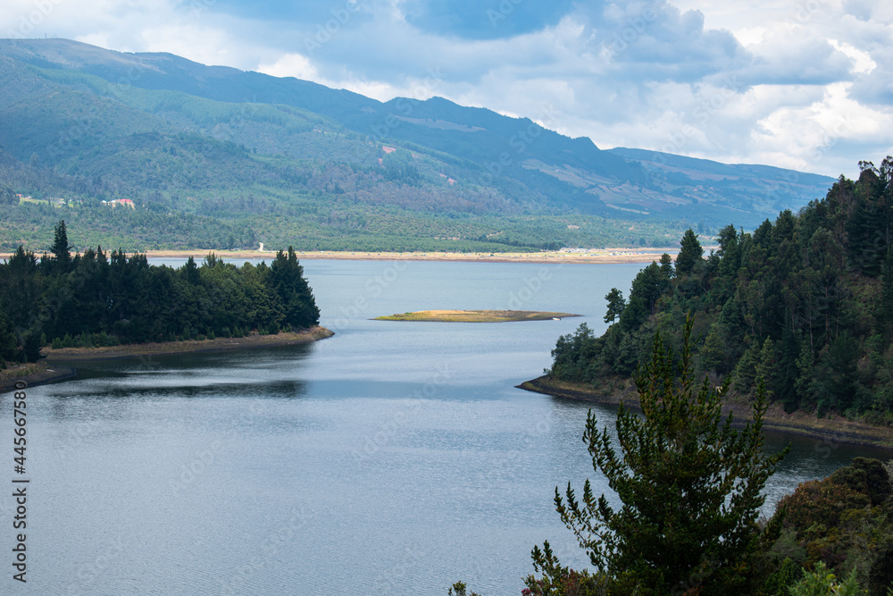 Neusa Reservoir in Colombia with a cloudy blue sky, mountains and forested areas.