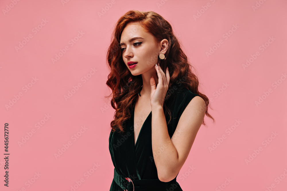 Portrait of curly woman in velvet dress on pink background. Wonderful lady with ginger wavy hair in dark green outfit posing.. Portrait of curly woman in velvet dress on pink background. Wonderful lady with ginger wavy hair in dark green outfit posing..