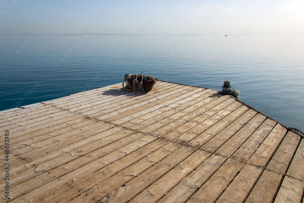 Fototapeta premium Travel. Pier on the sea. View at the sea from the wooden pier with posts and ropes with sparkling sea water