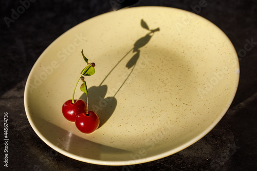 Two red sweet cherry fruit united together in dark shadow on yellow plate. Love peace creative healthy food cooking concept. Horizontal, copy space, top view