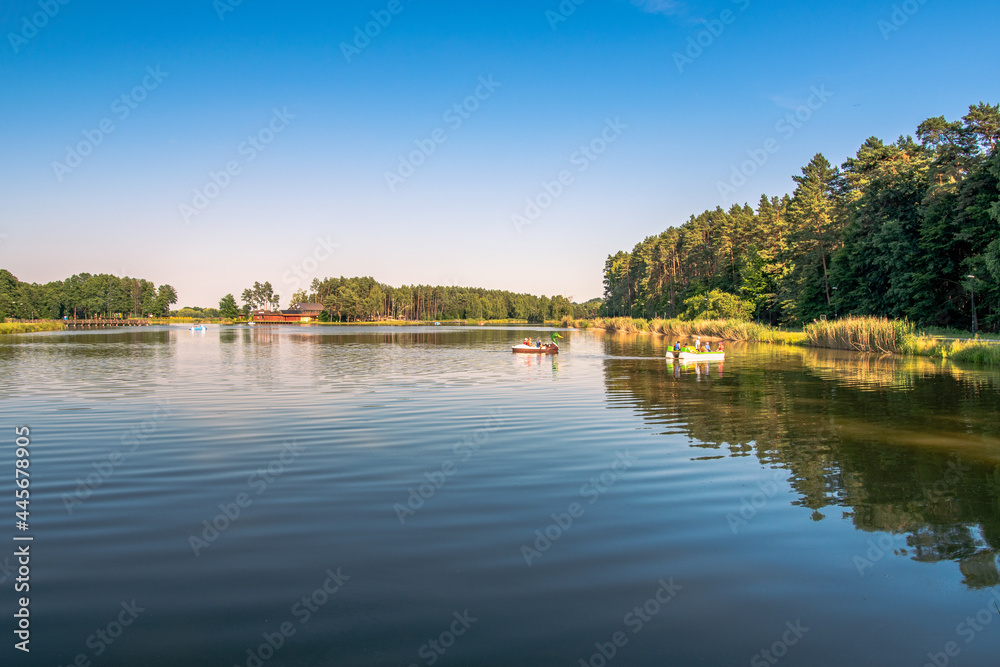 Beautiful lake landscape in the evening light. People swimming in pedalo boats. Forest and a wooden jetty in the background. Krasnobród, Roztocze, Poland.