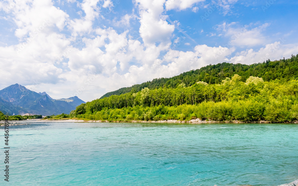 Aerial view of a crystal-clear river in the Alps in Germany under the blue sky and white clouds with lush trees on the shore, beautiful natural scenery