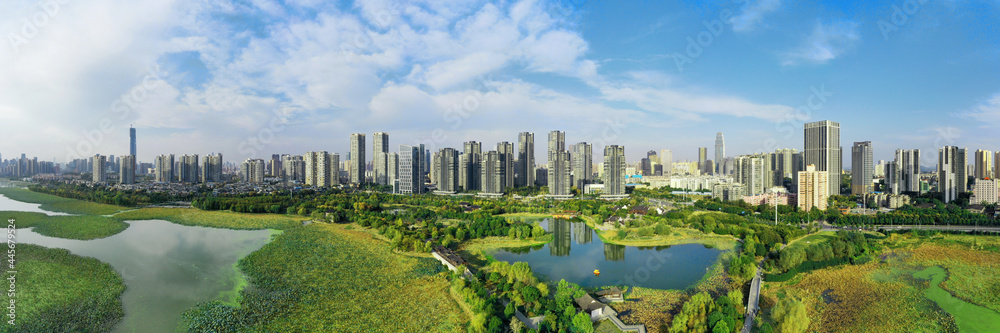 A green river by the city with tall buildings under the blue sky and white clouds, the combination of nature and modernity