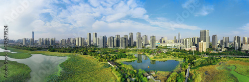 A green river by the city with tall buildings under the blue sky and white clouds, the combination of nature and modernity