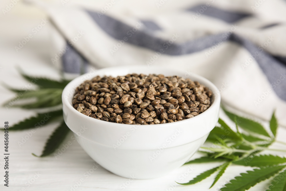 Bowl of hemp seeds and leaves on white table, closeup Bowl of hemp seeds and leaves on white table, closeup