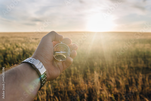 a man holds a compass in his hand while standing in a wheat field at sunset