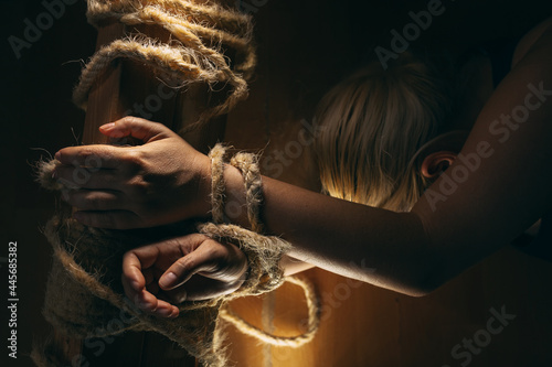 Fototapeta Blond woman tied to the wooden beam with shabby rope, lying on the floor