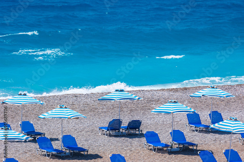 Colorful umbrellas and sunbeds on an empty beach resort - vacation concept on Greece islands in Aegean and Mediterranean seas