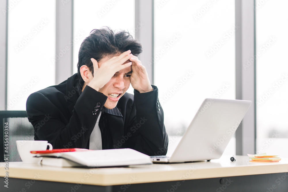 Stressed Asian businessman working with laptop in modern office. Young executive being angry about financial situation. Stressed Asian businessman working with laptop in modern office. Young executive being angry about financial situation.