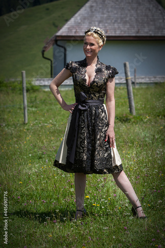 Blonde Frau im schwarzen Designer-Dirndl aus Spitze auf einer Bergwiese. photo