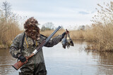a hunter stands in a lake with two dead ducks in his hand