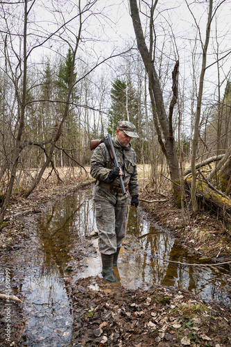 the hunter carefully crosses over a puddle on a forest road