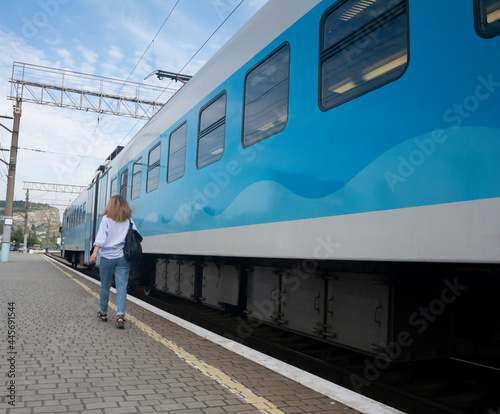 Beautiful young girl walks next to a blue train at the railway station perspective