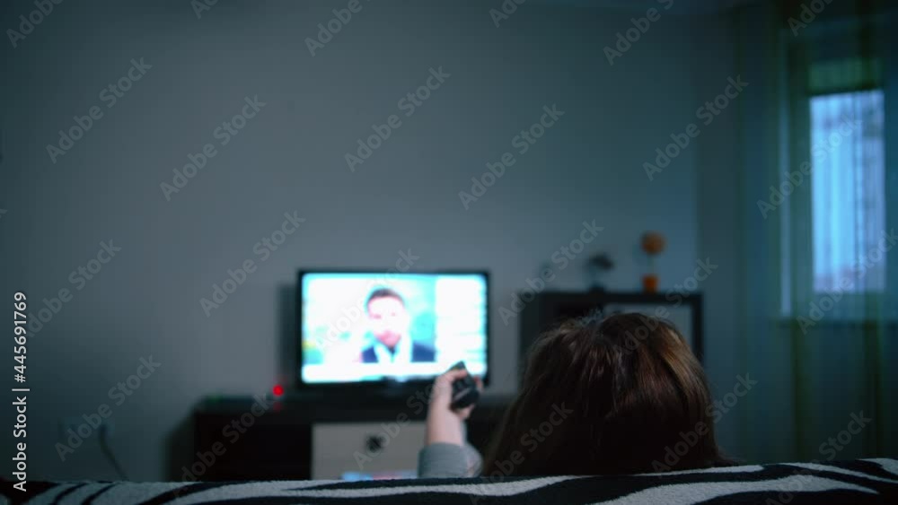woman switches tv channels in the evening, relaxing at home on the sofa, back view, cinematic shot