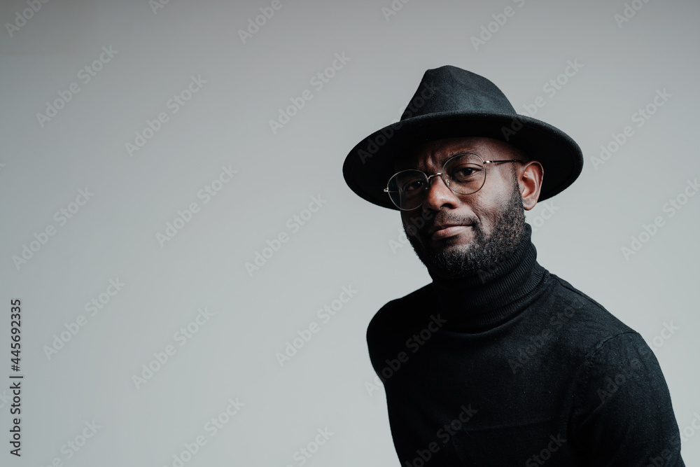 Attractive african american man wearing glasses and hat looking at camera while standing on gray background Attractive african american man wearing glasses and hat looking at camera while standing on gray background