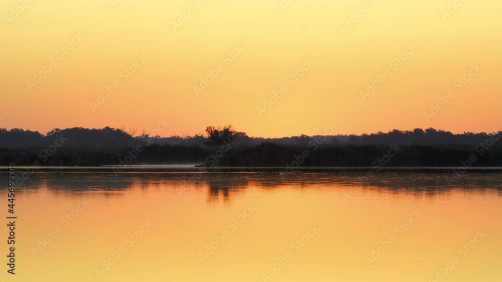 Early morning on calm river with fog. Sunrise over lake and beautiful morning landscape. Morning sun breaks through the thick fog. Fantastic foggy river in the golden sunlight on water surface Early morning on calm river with fog. Sunrise over lake and beautiful morning landscape. Morning sun breaks through the thick fog. Fantastic foggy river in the golden sunlight on water surface