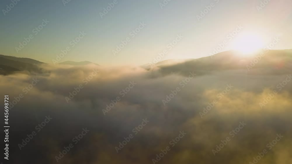 Aerial view of vibrant sunrise over white dense fog with distant dark silhouettes of mountain hills on horizon. Aerial view of vibrant sunrise over white dense fog with distant dark silhouettes of mountain hills on horizon.