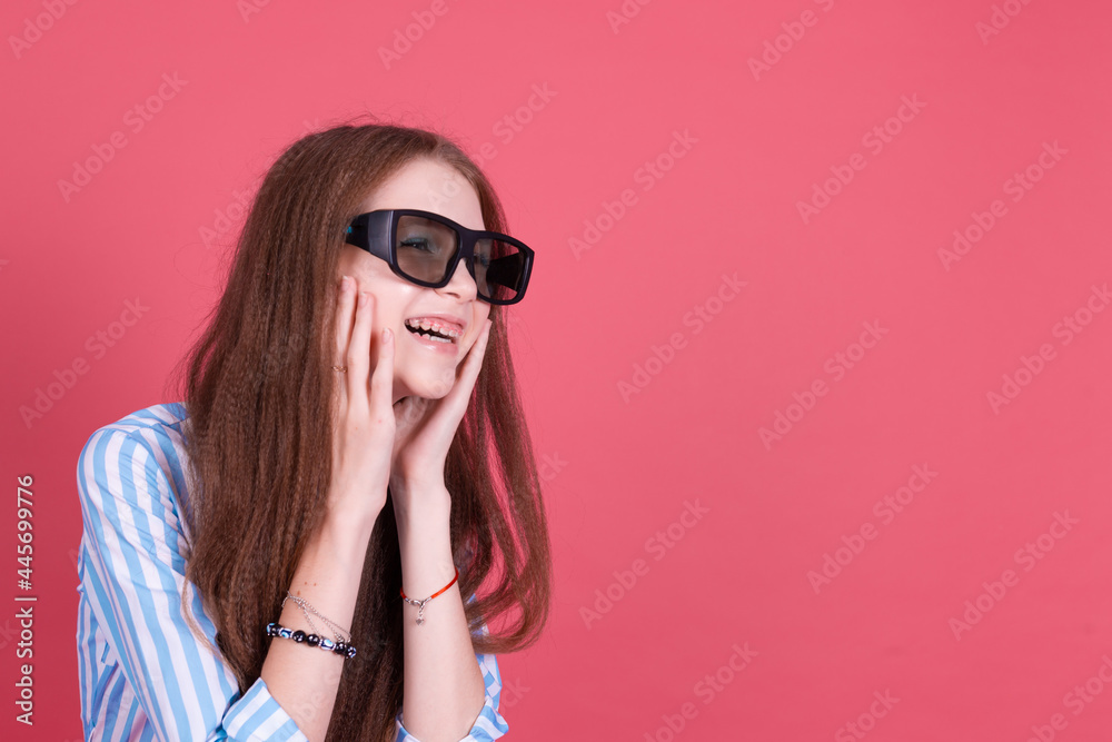 Fototapeta premium Little kid girl 13 years old in blue dress with brackets isolated on pink background wearing 3d cinema glasses happy smiling laugh