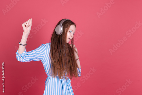 Little kid girl 13 years old in blue dress with brackets isolated on pink background in wireless headphones happy smiling dancing moving