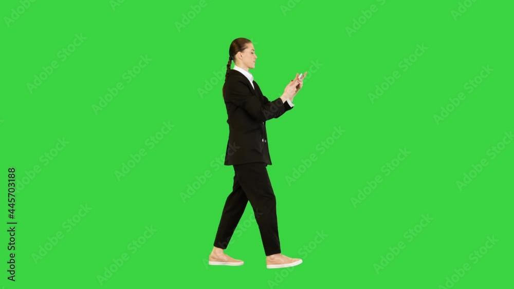 Young woman in office suit walking typing some text on her smartphone and smiling on a Green Screen, Chroma Key. Young woman in office suit walking typing some text on her smartphone and smiling on a Green Screen, Chroma Key.