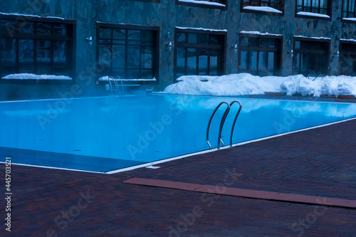 Swimming pool with blue warm water among snowdrifts near the hotel in winter