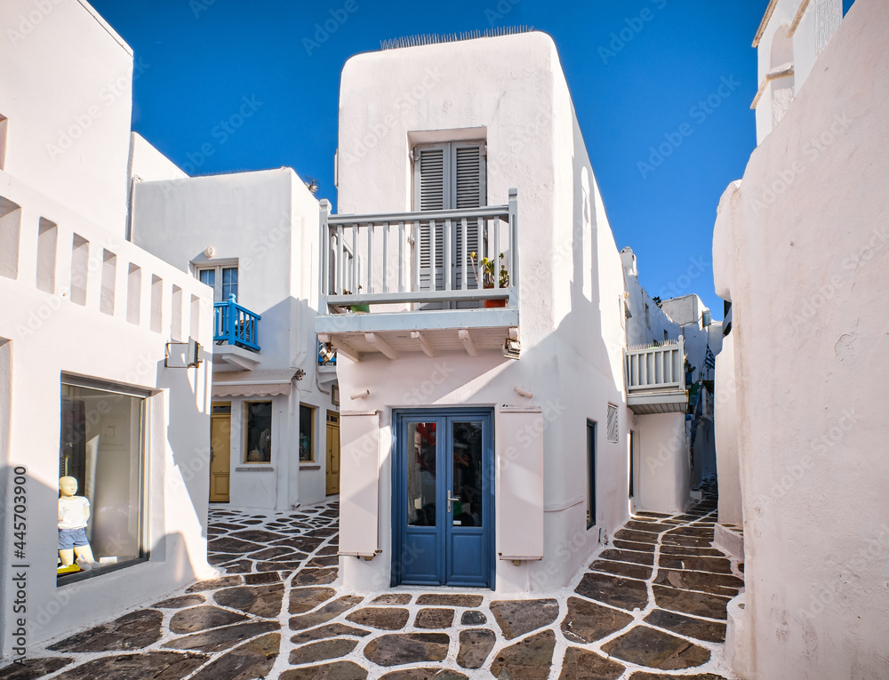 Traditional narrow cobbled streets, beautiful alleyways of Greek island town. Whitewashed houses, shop, cafe, morning summer sunshine. Mykonos, Greece