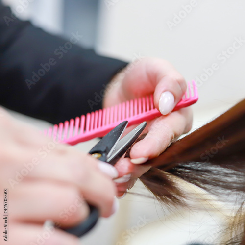 Stylist cutting split ends on her client at the salon. Close up. Square format.