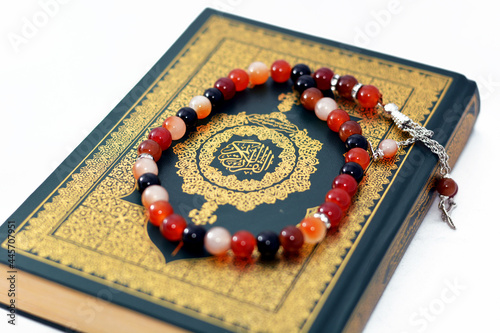 The holy Quran, Qur'an or Koran (the recitation) is the central religious text of Islam, believed by Muslims to be a revelation from God (Allah), isolated on white background with a rosary on it photo