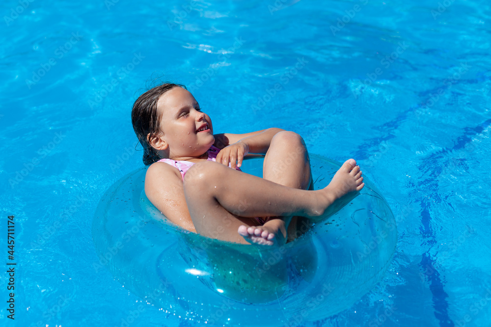 cheerful girl floating cross-legged and eyes closed on a blue inflatable circle in the hotel pool on a hot summer day. cheerful girl floating cross-legged and eyes closed on a blue inflatable circle in the hotel pool on a hot summer day.