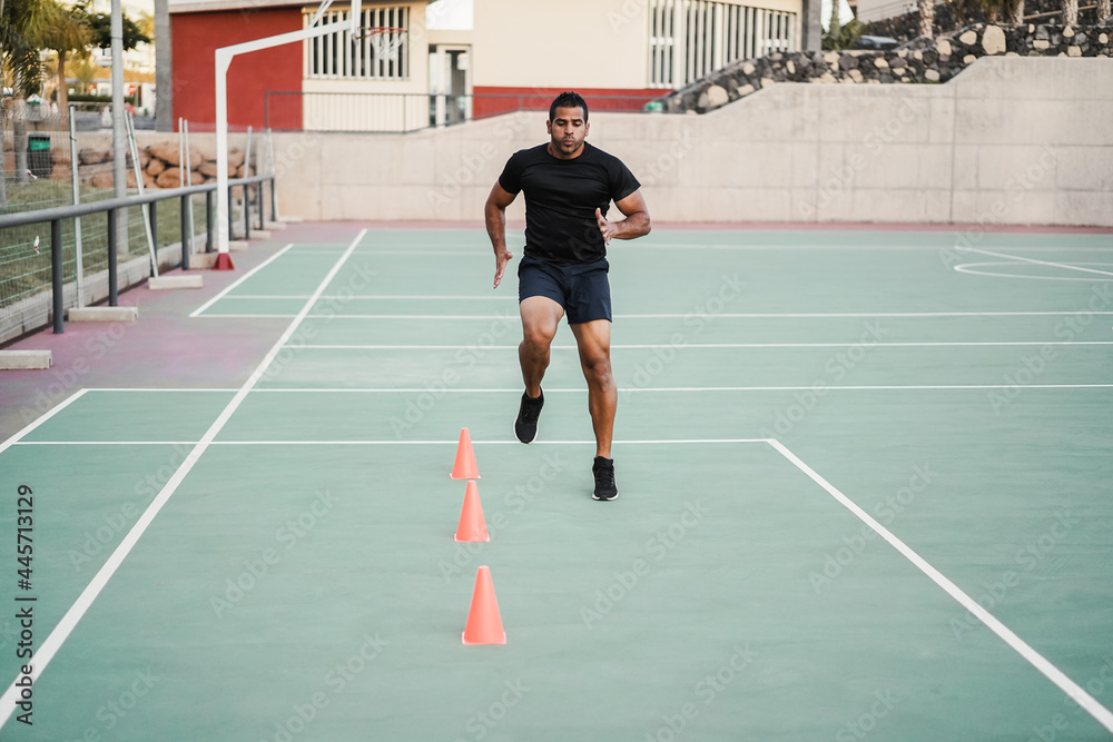 Hispanic man doing speed and agility cone drills workout session outdoors - Focus on man face