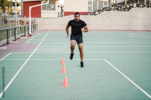 Hispanic man doing speed and agility cone drills workout session outdoors - Focus on man face © DisobeyArt
