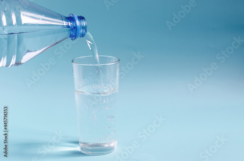 A plastic bottle that pours water into a glass glass on a colored background. A glass of clean water on a blue background close-up.