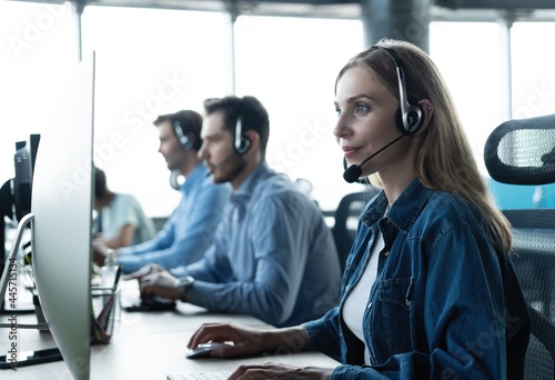 How can I help you? Beautiful call center workers in headphones are working at modern office photo