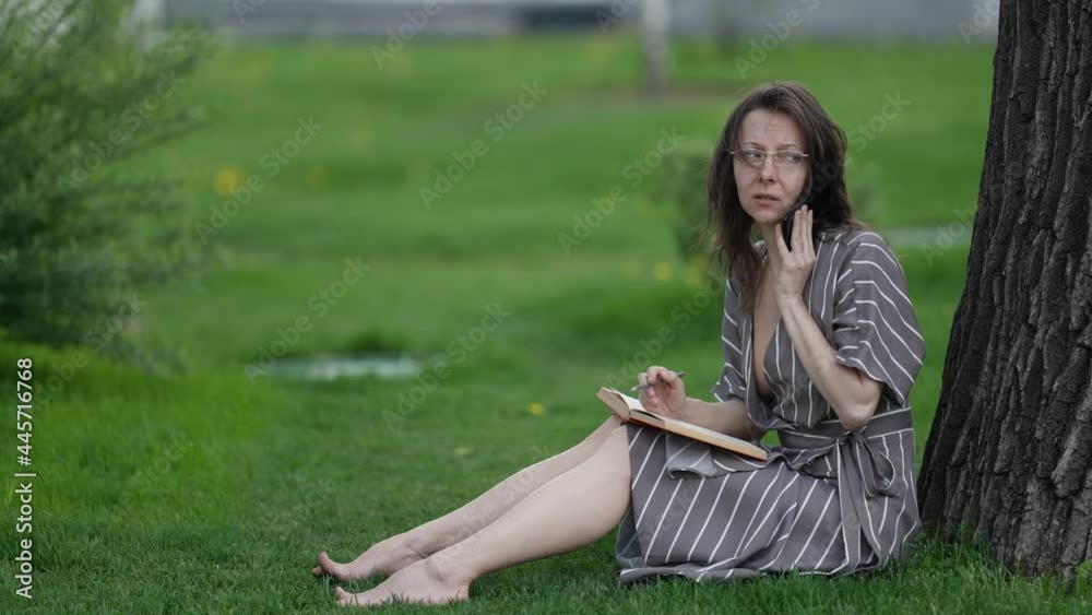 woman is negotiating by mobile phone during break or holiday in park at summer day woman is negotiating by mobile phone during break or holiday in park at summer day