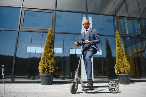businessman with electric scooter standing in front of modern business building talking on phone.