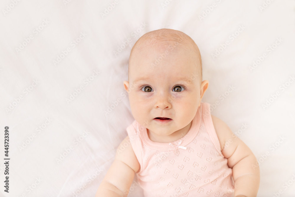 portrait of a baby girl in a crib in a pink bodysuit six months on a white cotton bed