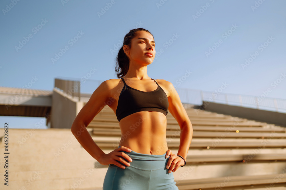 Fototapeta premium Young fitness woman exercising and stretching outdoors in the morning. Fit healthy athlete is doing workout on the street. Sport, Active life.