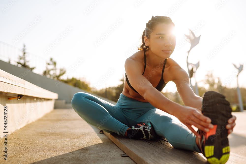 Young fitness woman exercising and stretching outdoors in the morning. Fit healthy athlete is doing workout on the street. Sport, Active life.