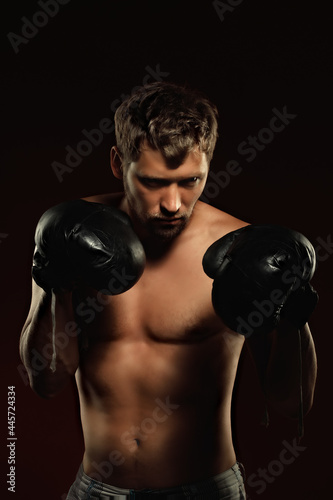 This is a dramatic portrait of a boxer in old boxing gloves on a dark background. An athletic mixed martial arts fighter stands in a fighting stance. Banner for sports events.