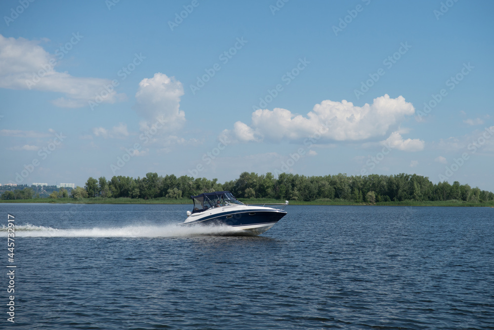 Obraz premium A motor boat cruises on the water against the background of an island overgrown with green trees.
