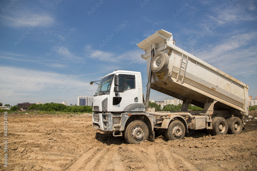 dump truck at work at a construction site. The process of transporting unloading soil on a construction machine. dump truck with raised body. Commercial vehicles dump truck at work at a construction site. The process of transporting unloading soil on a construction machine. dump truck with raised body. Commercial vehicles