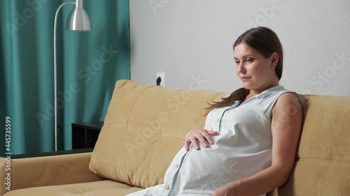 Pregnant woman doing breathing exercise experiencing contractions while sitting on the couch. photo
