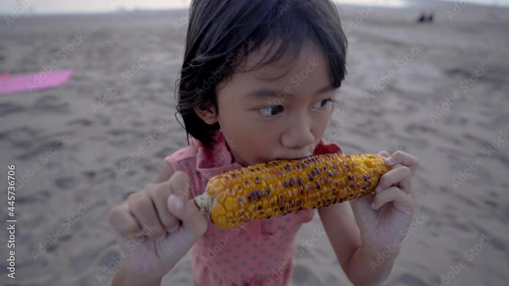 Adorable funny girl eating corn on the cob on sunny summer day