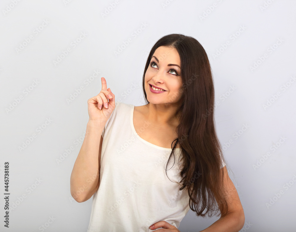 Beautiful excited casual woman pointing the finger up with toothy smiling on empty copy space Beautiful excited casual woman pointing the finger up with toothy smiling on empty copy space