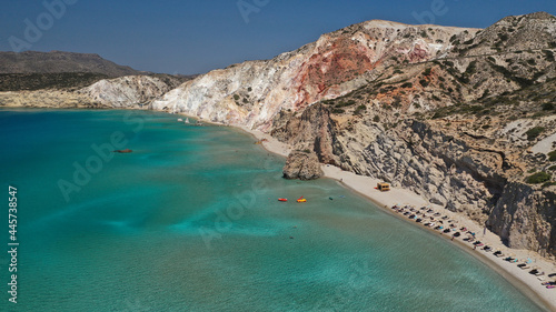 Aerial drone view of iconic volcanic white chalk sandy organised with sun beds and umbrellas beach of Firiplaka with turquoise clear sea and rocky colour formations, Milos island, Cyclades, Greece
