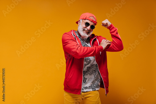 Bilde på lerret Smiling man in red cap demonstrates biceps on orange background