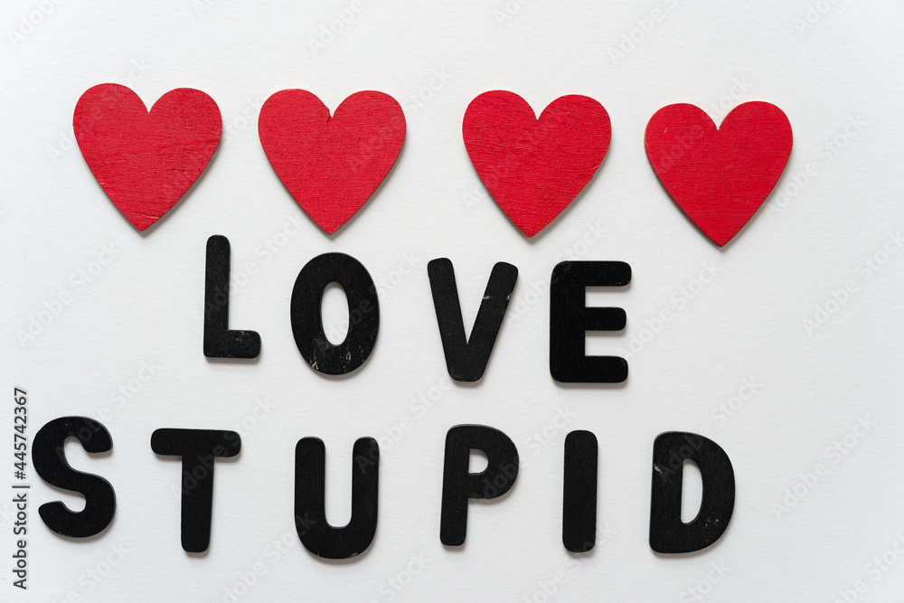 black chalk letters loosely arranged to read love stupid and 4 hand painted red hearts on a white background
